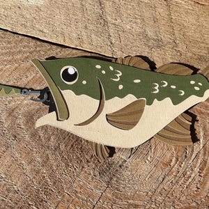 May include: A green and brown paper craft of a bass fish with a lure in its mouth.
