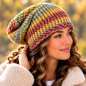 May include: A slouchy knit beanie featuring a variegated yarn pattern with horizontal stripes in shades of burgundy, mustard yellow, olive green, and grey. The hat has a thick, textured stitch construction with a folded brim edge.