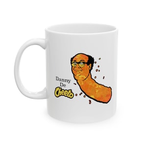 May include: White ceramic mug featuring a cartoon illustration of Danny DeVito as a Cheeto. The text "Danny De Cheeto" is printed on the mug.