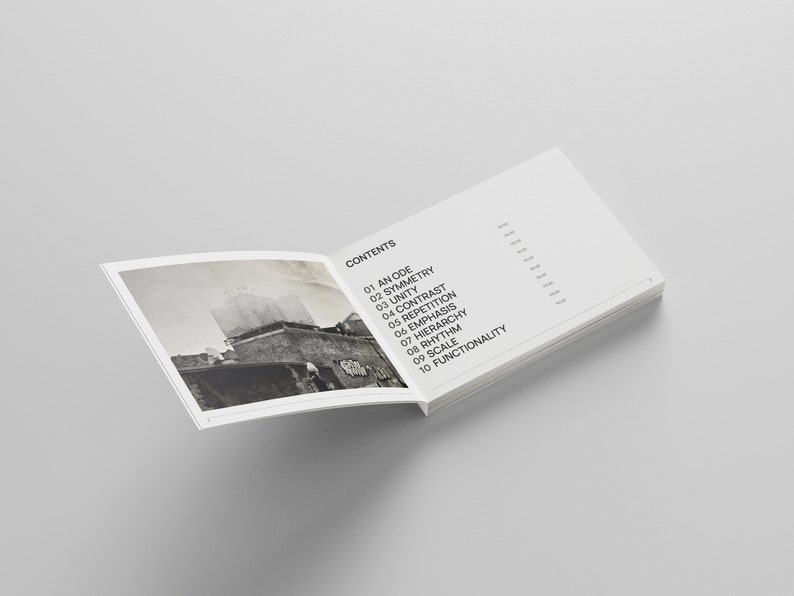 May include: An open book with a black and white photo on the left page and a list of design principles on the right page. The list includes: An Ode, Symmetry, Unity, Contrast, Repetition, Emphasis, Hierarchy, Rhythm, Scale, and Functionality.