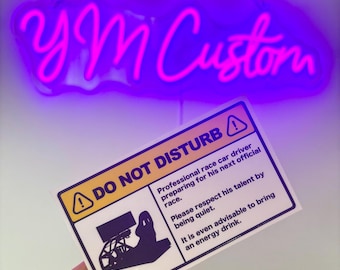 May include: A rectangular white sign with black text and a yellow warning icon. The sign reads DO NOT DISTURB, Professional race car driver preparing for his next official race. Please respect his talent by being quiet. It is even advisable to bring an energy drink. A black graphic of a racing simulator setup is included.