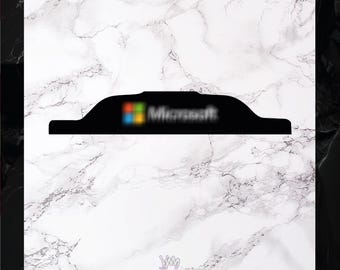 May include: A black, horizontal, elongated, and curved plastic-like object featuring the Microsoft logo with its signature four-colored square icon and the text "Microsoft" in white, positioned centrally on a white marble-patterned background.