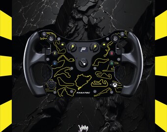 May include: Black racing wheel featuring yellow track outlines and buttons. The wheel has the word "FANATEC" printed on it. The background is black with a yellow and black border.