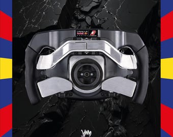 May include: A black and silver racing wheel featuring the text "ORACLE RED BULL RACING" and a logo. The wheel has a complex design with multiple buttons and grips. The background is a dark, textured surface.