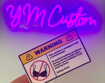 May include: A rectangular sticker with a yellow top section containing the word WARNING and a triangle icon. The white lower section features a red circle with a line through a bra icon and text stating: This vehicle is equipped with a turbocharger. To avoid breathing problems during strong acceleration, women are prohibited from wearing bras. Safety first!