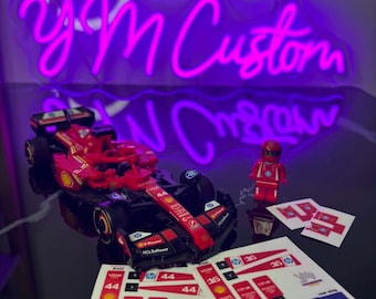 May include: A red and black toy race car with sponsor decals, a red Lego figure, and a sheet of decals. A purple neon sign in the background reads "yom Custom".