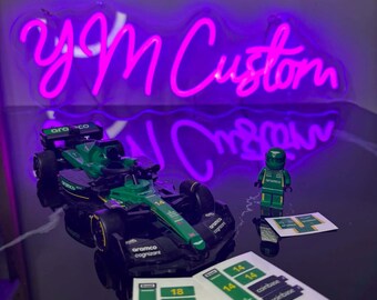 May include: A green and black toy race car with the number 14 on it, a Lego figure, and stickers. The neon sign in the background says "yM Custom".