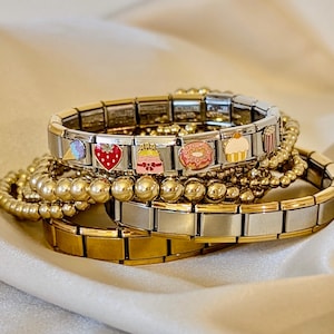 May include: A stack of charm bracelets with gold and silver links. The charms are colorful and feature various sweet treats, including a cupcake, donut, ice cream cone, strawberry, and cake.