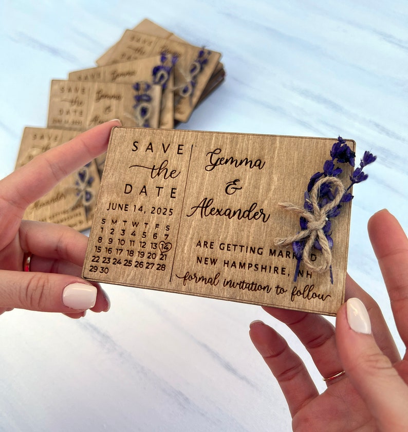 May include: Wooden save the date card with a calendar showing June 14, 2025, with a heart marking the date. The card also includes the text "Save the Date", "Gemma & Alexander", "Are getting married", "New Hampshire, NH", and "Formal invitation to follow".