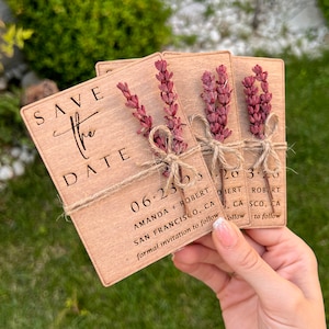 May include: Three wooden save the date cards with a rustic brown finish. Each card has a small bundle of dried lavender tied with twine. The text on the cards reads "Save the Date", "06.23.23", "Amanda + Robert", "San Francisco, CA", and "Formal invitation to follow".