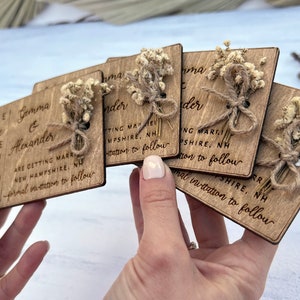 May include: Set of six wooden save the date cards with dried flowers and twine. The cards are engraved with the text "Save the Date", the couple's names, the date, and the location of the wedding. The cards are perfect for a rustic or farmhouse wedding.