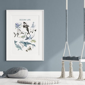 Op de afbeelding: Een witte ingelijste print met de titel "Ocean Life" met aquarel illustraties van verschillende zeedieren, waaronder een octopus, walvis, haai, dolfijn en zeeschildpad.