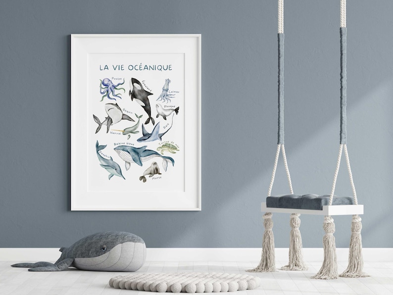 May include: A framed watercolor print titled "LA VIE OC&Eacute;ANIQUE" featuring various marine animals, including an octopus, orca, and shark. A plush whale and a swing with tassels are in the foreground.
