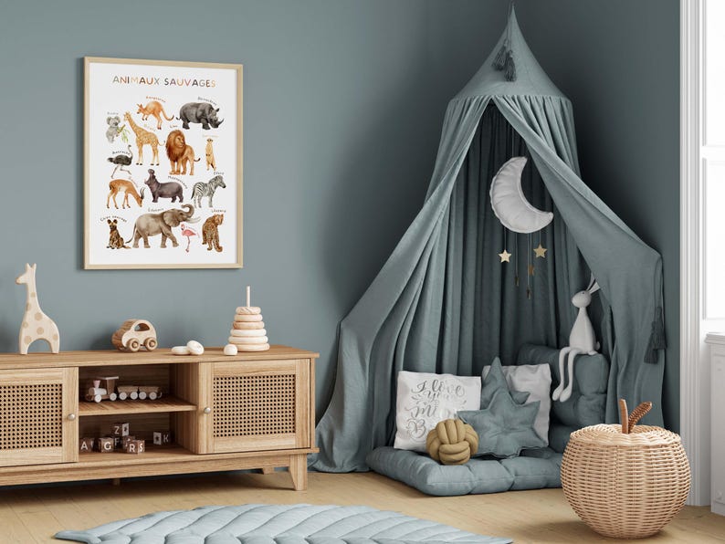 May include: A framed poster with the text "ANIMAUX SAUVAGES" displays watercolor illustrations of various animals. A wooden cabinet holds toys, and a canopy bed with a moon and stars hangs in the corner. The room is decorated in shades of blue and beige.