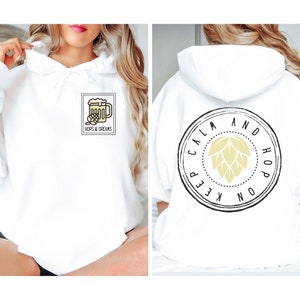 Op de afbeelding: Witte hoodie met een afbeelding van een bierglas en de tekst "Hops & Dreams" op de voorkant. De achterkant van de hoodie heeft een ronde afbeelding met de tekst "Keep Calm and Hop On".