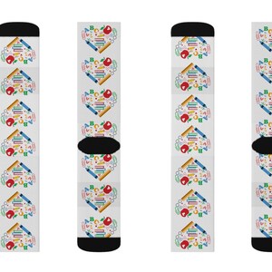 May include: Four pairs of white socks with a colorful pattern of school supplies, including pencils, crayons, rulers, and an apple. The socks have a black cuff and toe.