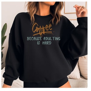 Może przedstawiać: Czarna bluza z nadrukiem graficznym, który głosi "Coffee because adulting is hard".
