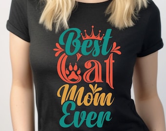 May include: Black t-shirt with the text "Best Cat Mom Ever" in teal, orange, and yellow. The design includes a crown, a cat paw print, and floral accents. The shirt is a crew neck and has rolled-up sleeves.