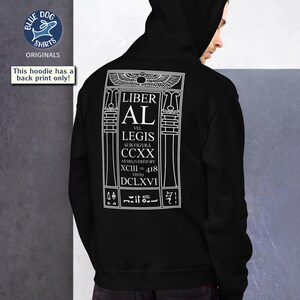 Puede incluir: Sudadera con capucha negra con un gr&aacute;fico blanco en la espalda. El gr&aacute;fico incluye el texto "LIBER AL VEL LEGIS" y otro texto en un dise&ntilde;o estilizado. La sudadera tiene capucha y est&aacute; hecha de un material suave.