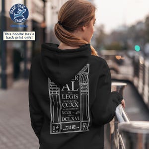 Puede incluir: Sudadera con capucha negra con un estampado gr&aacute;fico blanco en la espalda. El estampado incluye el texto "AL VEL LEGIS SUB FIGVRA CCXX AS DELIVERED BY XCIII=418 VINTO DCLXVI". La sudadera tambi&eacute;n tiene capucha y bolsillo canguro.