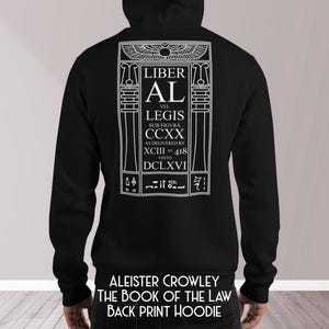 Puede incluir: Sudadera con capucha negra con un gr&aacute;fico blanco en la espalda. El gr&aacute;fico incluye el texto "LIBER AL VEL LEGIS" y otro texto en un marco rectangular. El texto "ALEISTER CROWLEY THE BOOK OF THE LAW BACK PRINT HOODIE" est&aacute; impreso en la parte inferior.