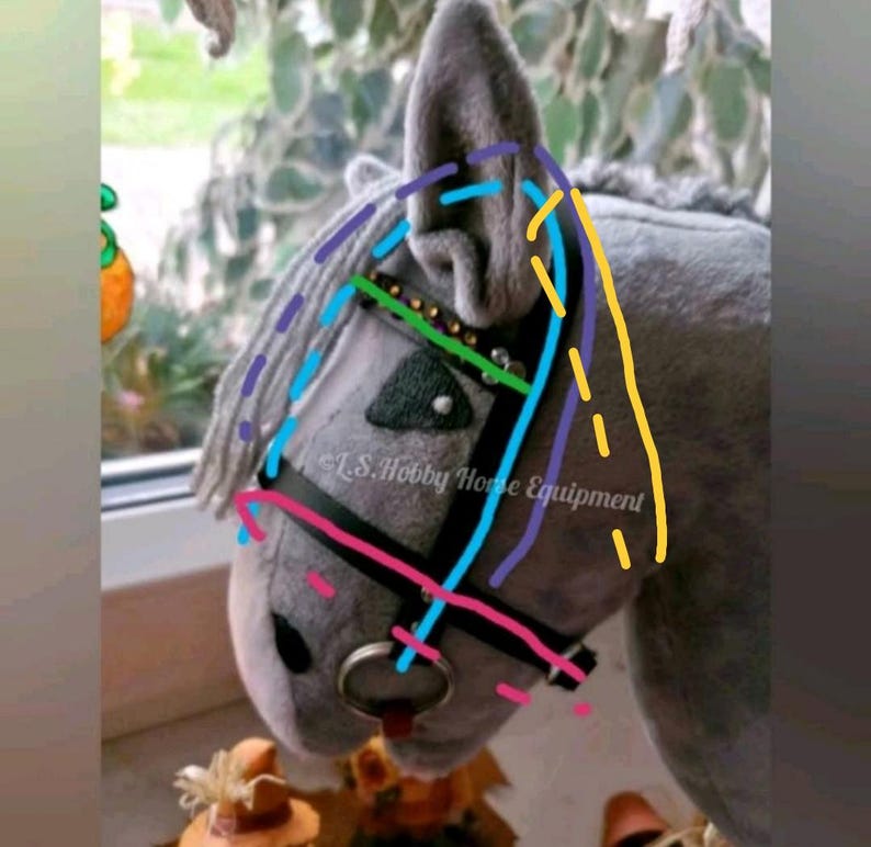 K&ouml;nnte beinhalten: Ein graues Steckenpferd mit einem schwarzen Zaumzeug und Z&uuml;geln. Die M&auml;hne des Pferdes ist wei&szlig; und das Ohr ist grau. Das Zaumzeug hat ein blaues, gr&uuml;nes, violettes und gelbes N&auml;hmuster. Der Text "L.S. Hobby Horse Equipment" ist auf dem Zaumzeug sichtbar.