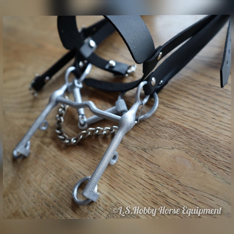 K&ouml;nnte beinhalten: Ein silberfarbenes Gebiss f&uuml;r ein Hobbypferd, mit einem schwarzen Lederhalfter und Z&uuml;geln. Das Gebiss hat eine Kandare und ein Gebissst&uuml;ck. &copy; L.S. Hobby Horse Equipment