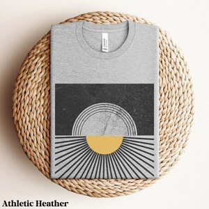 May include: A gray t-shirt with a black and yellow graphic design of a sun with rays. The design has a distressed look.