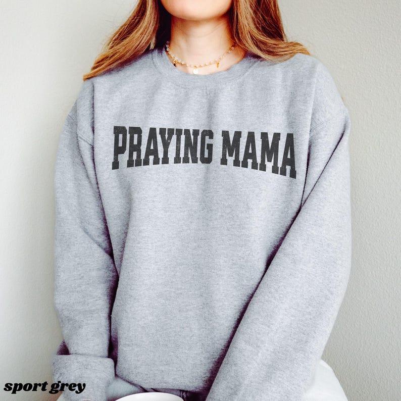 Pode incluir: Uma camisa de moletom cinza com o texto "Praying Mama" impresso em preto.