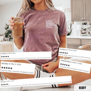 Puede incluir: Una camiseta malva con el texto "Late-Night Reading Club" en blanco. La persona que lleva la camiseta sostiene un vaso con una pajita y una bebida. La persona est&aacute; sentada en una silla con calcetines a rayas blancas y negras.