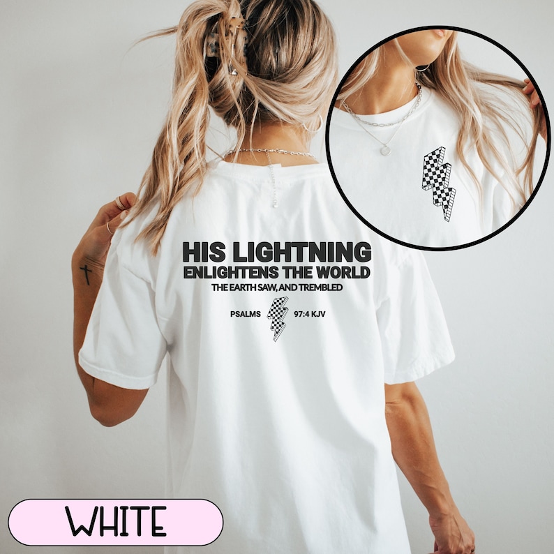 May include: White t-shirt with the text "HIS LIGHTNING ENLIGHTENS THE WORLD" and "PSALMS 97:4 KJV" printed in black. The shirt features a checkered lightning bolt graphic. The shirt is a casual wear item.