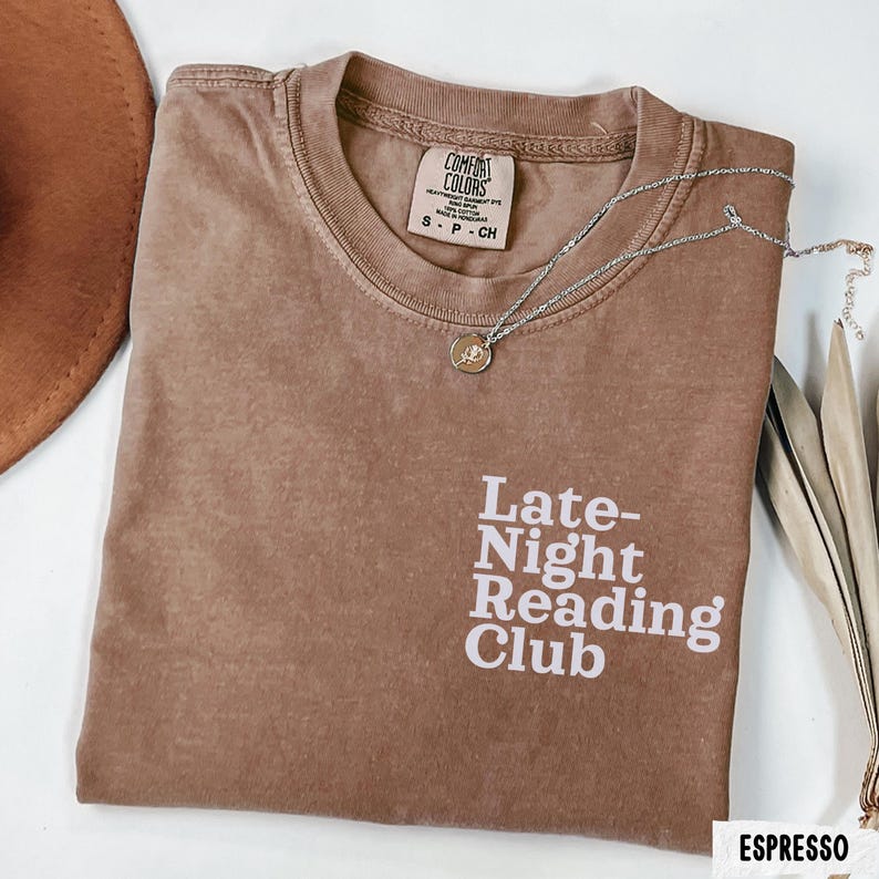 Puede incluir: Una camiseta marr&oacute;n con el texto "Late-Night Reading Club" en blanco. La camiseta tiene un aspecto desgastado y est&aacute; hecha de una tela suave y c&oacute;moda.