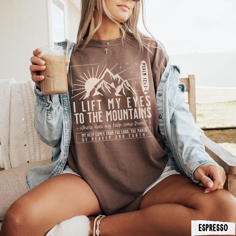 May include: Espresso-colored t-shirt with the text "I lift my eyes to the mountains" and a mountain graphic. The shirt also includes the text "My help comes from the Lord, the maker of heaven and earth."