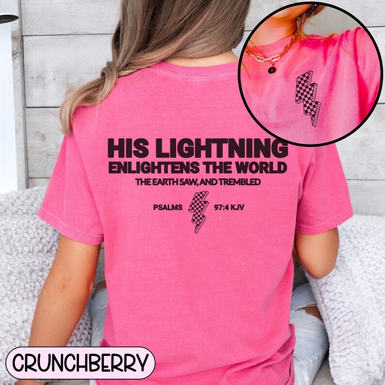 May include: A bright pink t-shirt with the text "HIS LIGHTNING ENLIGHTENS THE WORLD THE EARTH SAW, AND TREMBLED PSALMS 97:4 KJV" printed on the back. A checkered lightning bolt graphic is also featured. The brand name "CRUNCHBERRY" is at the bottom.