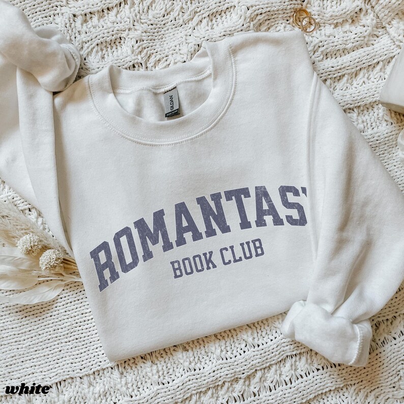 May include: White crewneck sweatshirt with the text "ROMANTAS BOOK CLUB" in purple lettering.