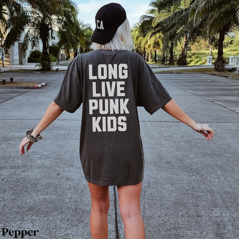 May include: A person wearing a dark gray t-shirt with the text "LONG LIVE PUNK KIDS" printed in white. The person is wearing a black baseball cap with the letter "CA" on it.