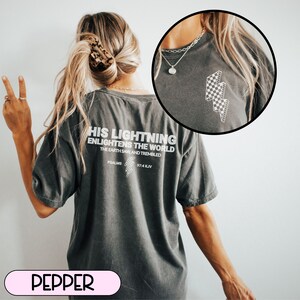 May include: A dark gray t-shirt with white text on the back that reads "HIS LIGHTNING ENLIGHTENS THE WORLD." The shirt also features a checkered lightning bolt design. The text "PSALMS 97:4 KJV" is below the main text.