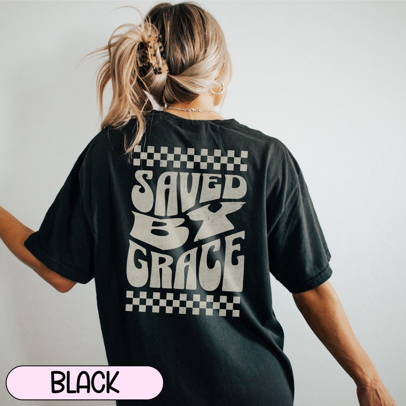 May include: Black oversized t-shirt with a white graphic that says "Saved by Grace" with a checkered pattern above and below the text.