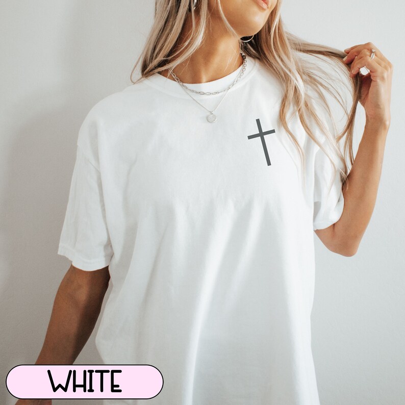 May include: White t-shirt with a simple black cross graphic on the front.