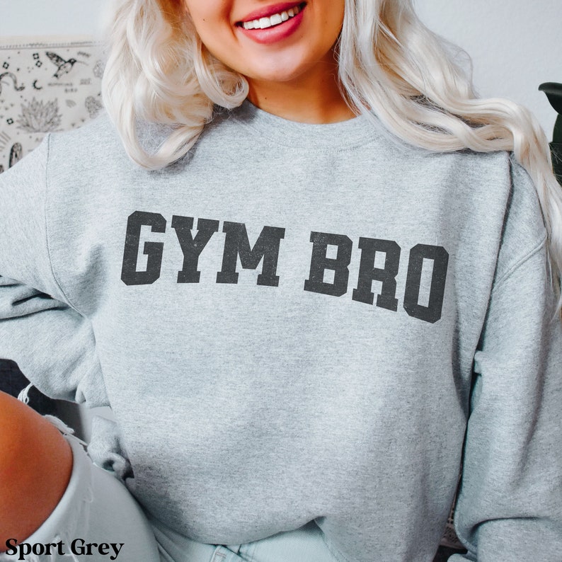 May include: Sport grey sweatshirt with the text "GYM BRO" in black block letters. The sweatshirt is a light grey color.