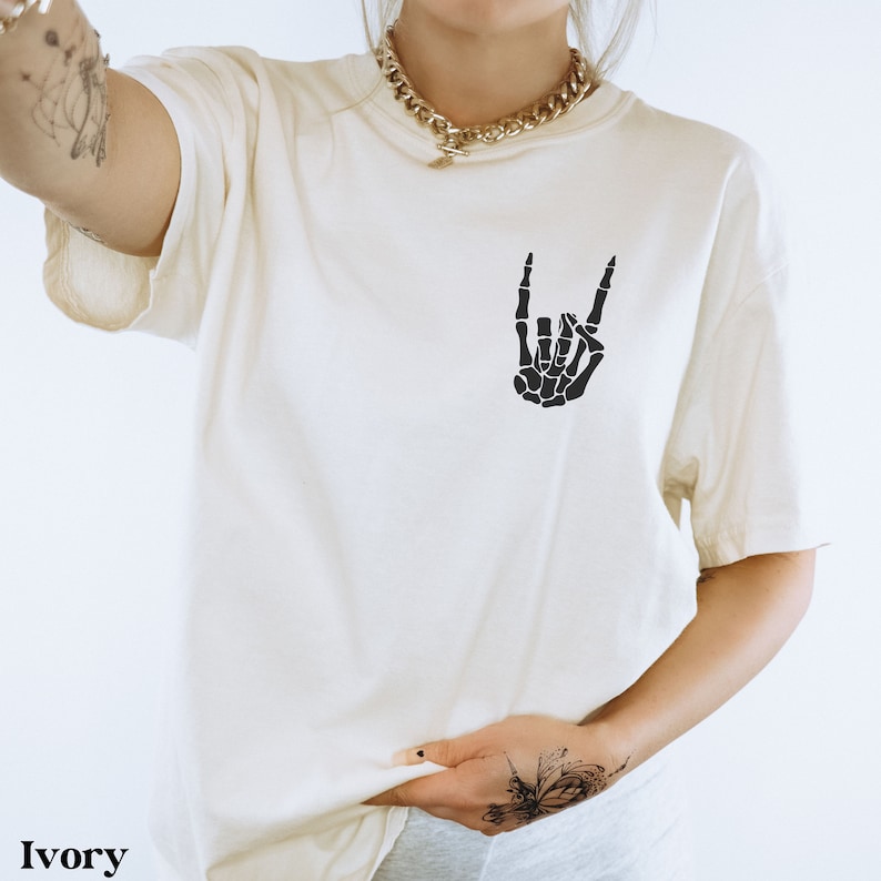 May include: Ivory t-shirt with a black skeleton hand making a rock and roll sign.