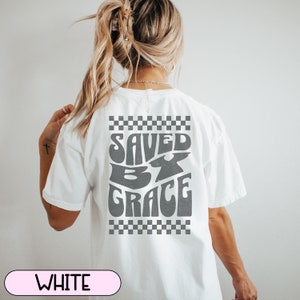 May include: White t-shirt with a checkered pattern and the text "SAVED BY GRACE" in a retro font.