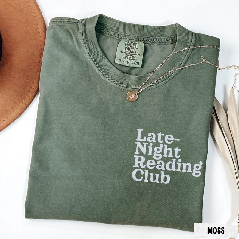 Puede incluir: Una camiseta verde musgo con el texto "Late-Night Reading Club" en blanco. La camiseta est&aacute; hecha de una tela suave y c&oacute;moda y tiene un corte holgado.