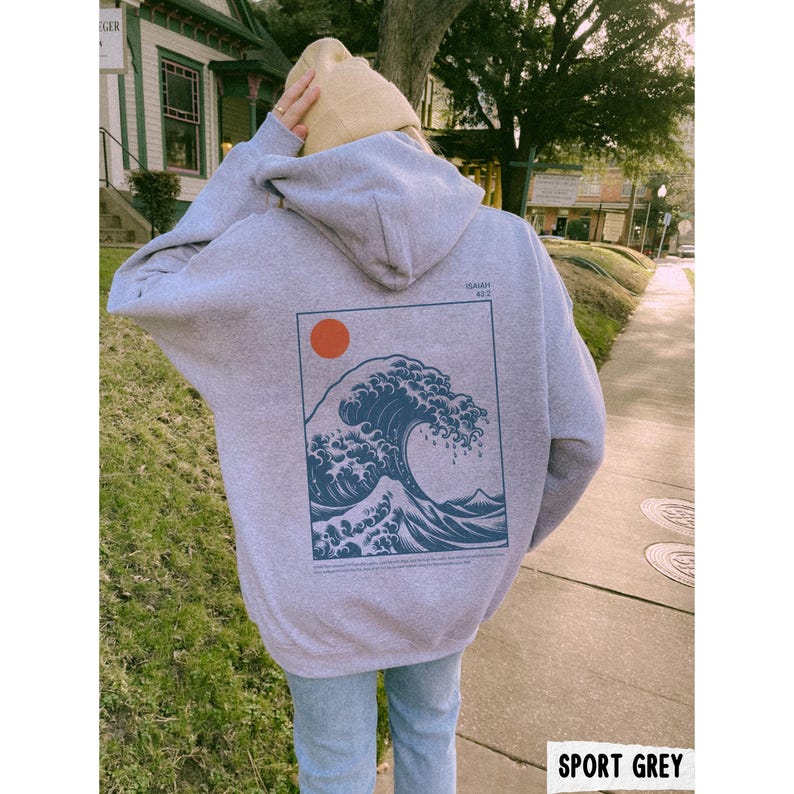 May include: Sport grey hoodie with a large graphic on the back featuring a blue wave design, a red sun, and text. The hoodie has a hood and is worn with blue jeans. The text "SPORT GREY" is at the bottom of the image.