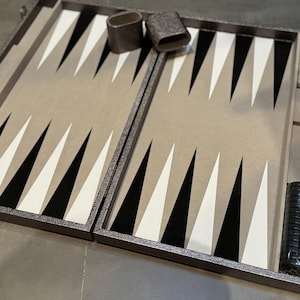 以下が含まれることがあります： ハンドル付きのグレーのキャリーケースに入った白黒のバックギャモンゲームセット。ケースの内側には白黒のチェッカーボードのデザインが施されています。