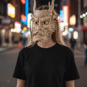 Può includere: Maschera da drago beige con dettagli intricati, tra cui corna e un volto dettagliato. La persona indossa una maglietta nera e jeans. Lo sfondo è una strada cittadina sfocata di notte.