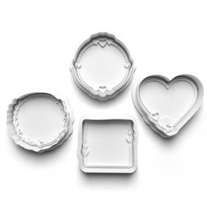 May include: Four white plastic cookie cutters in the shapes of a heart, a square, a circle, and a circle with a decorative border. Each cutter has a small heart design on the inside.