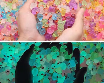 Könnte beinhalten: Eine Hand hält eine große Gruppe bunter Gummibadenten. Die Enten sind alle in verschiedenen Farben und haben unterschiedliche Designs. Einige der Enten leuchten im Dunkeln.
