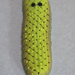 May include: A lime green, elongated object with a textured, geometric pattern. Two black, circular eyes are near the top. The object has a rounded shape and a slightly darker green hue at the base.