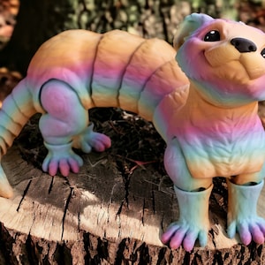 Op de afbeelding: Een kleurrijk, regenbooggekleurd, gearticuleerd frettenbeeldje met een glimlachend gezicht. Het beeldje is gemaakt van een glad, plastic-achtig materiaal en heeft een lange, slanke staart.